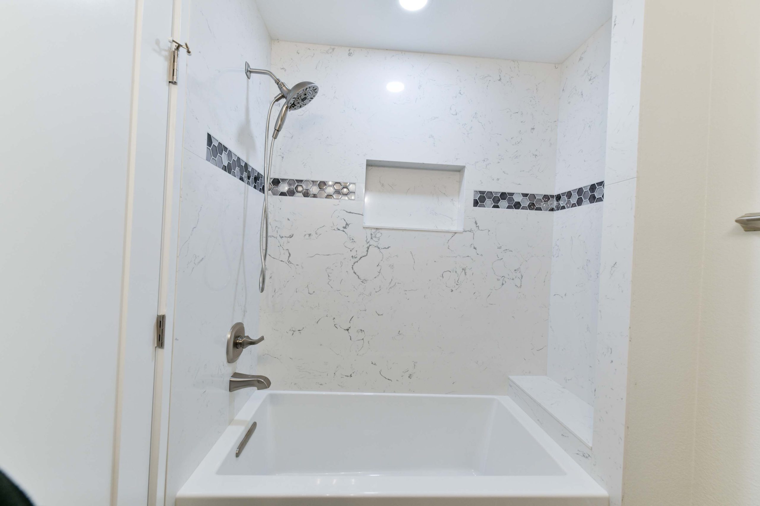 Full bathroom renovation featuring a new tub and shower combination with seamless solid-surface wall panels, built-in shower niche, and modern brushed nickel fixtures for a clean, low-maintenance finish.