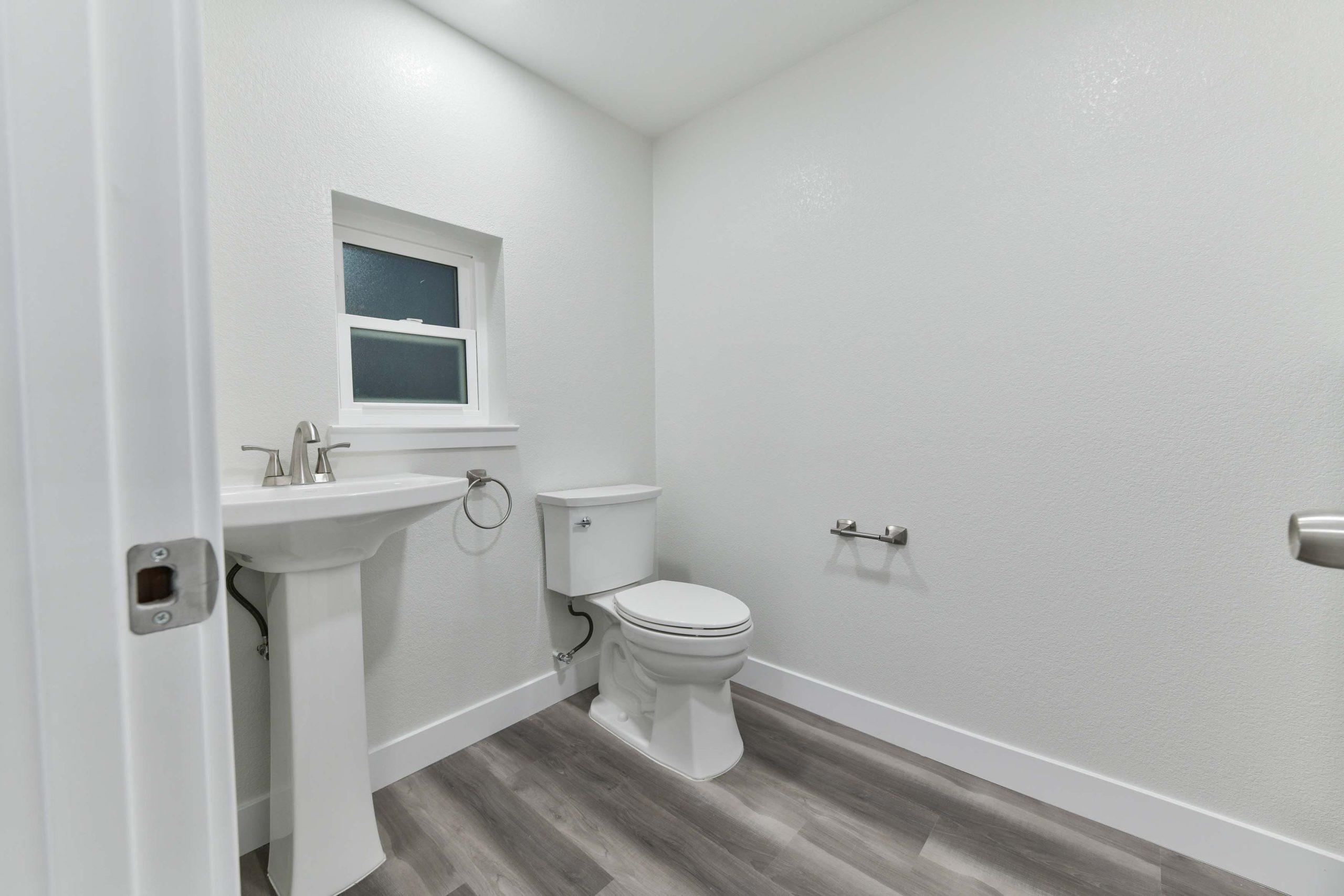 Renovated half bathroom featuring a classic pedestal sink, new toilet, updated fixtures, fresh paint, and continuous flooring that ties in with the rest of the home.