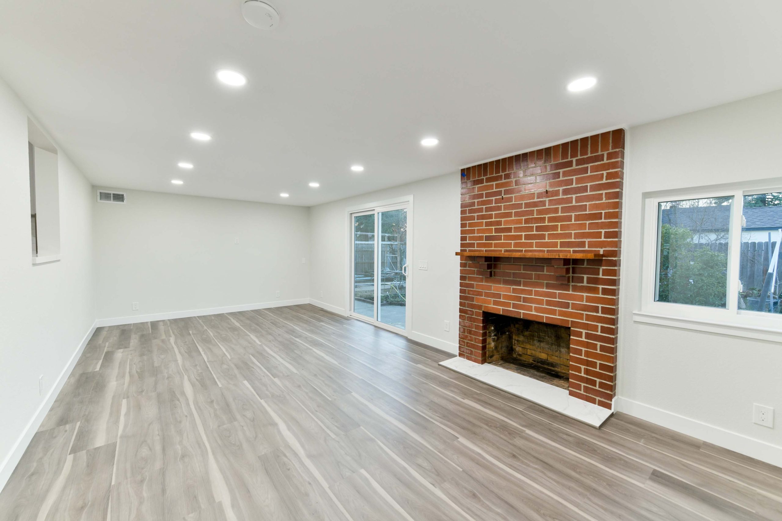 Refinished living area featuring new flooring, recessed lighting, fresh paint, and a restored brick fireplace preserved as a focal point during the renovation.