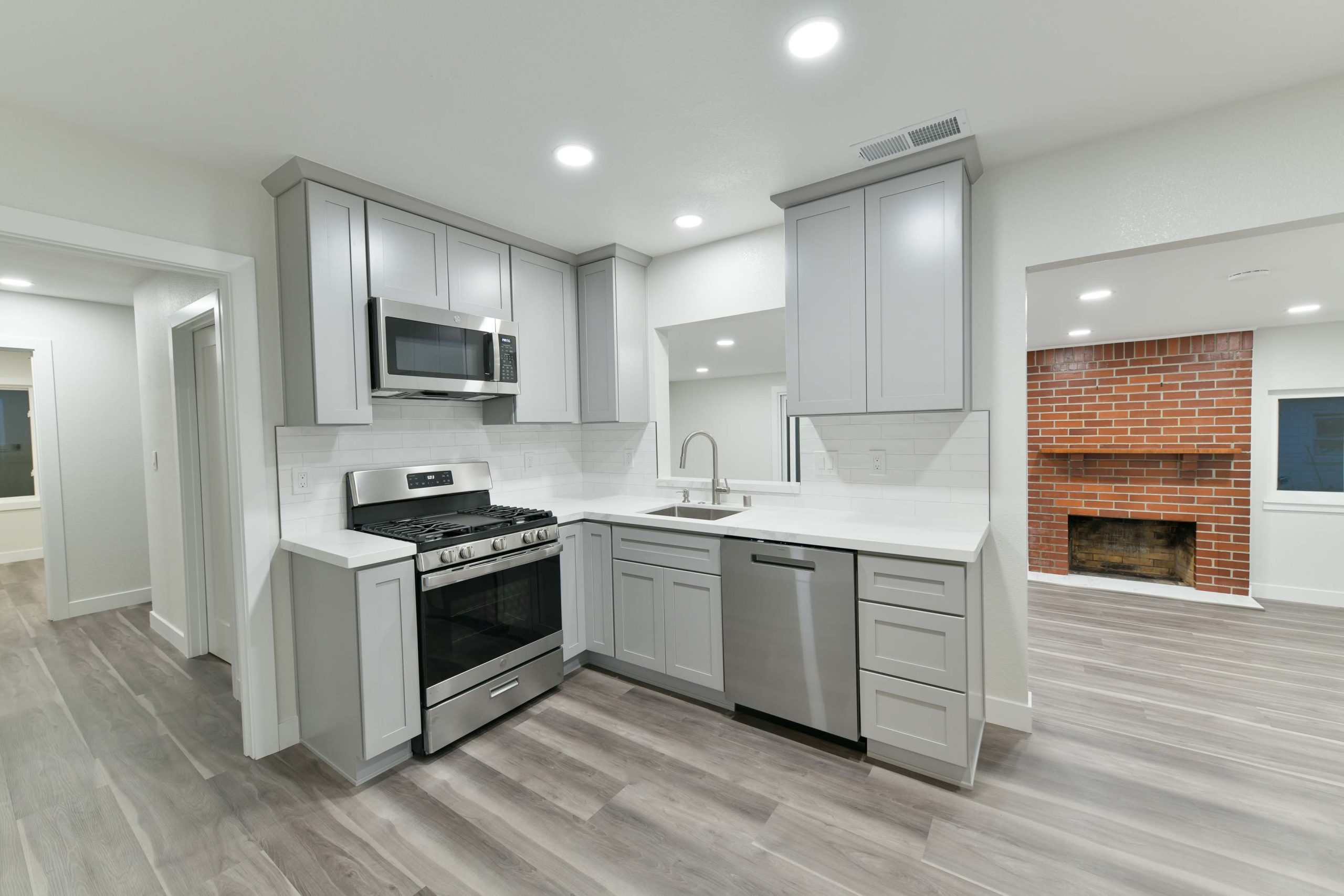 Open-concept kitchen after a full home renovation in Sacramento, featuring gray shaker cabinets, white quartz countertops, recessed lighting, and durable luxury vinyl plank flooring.