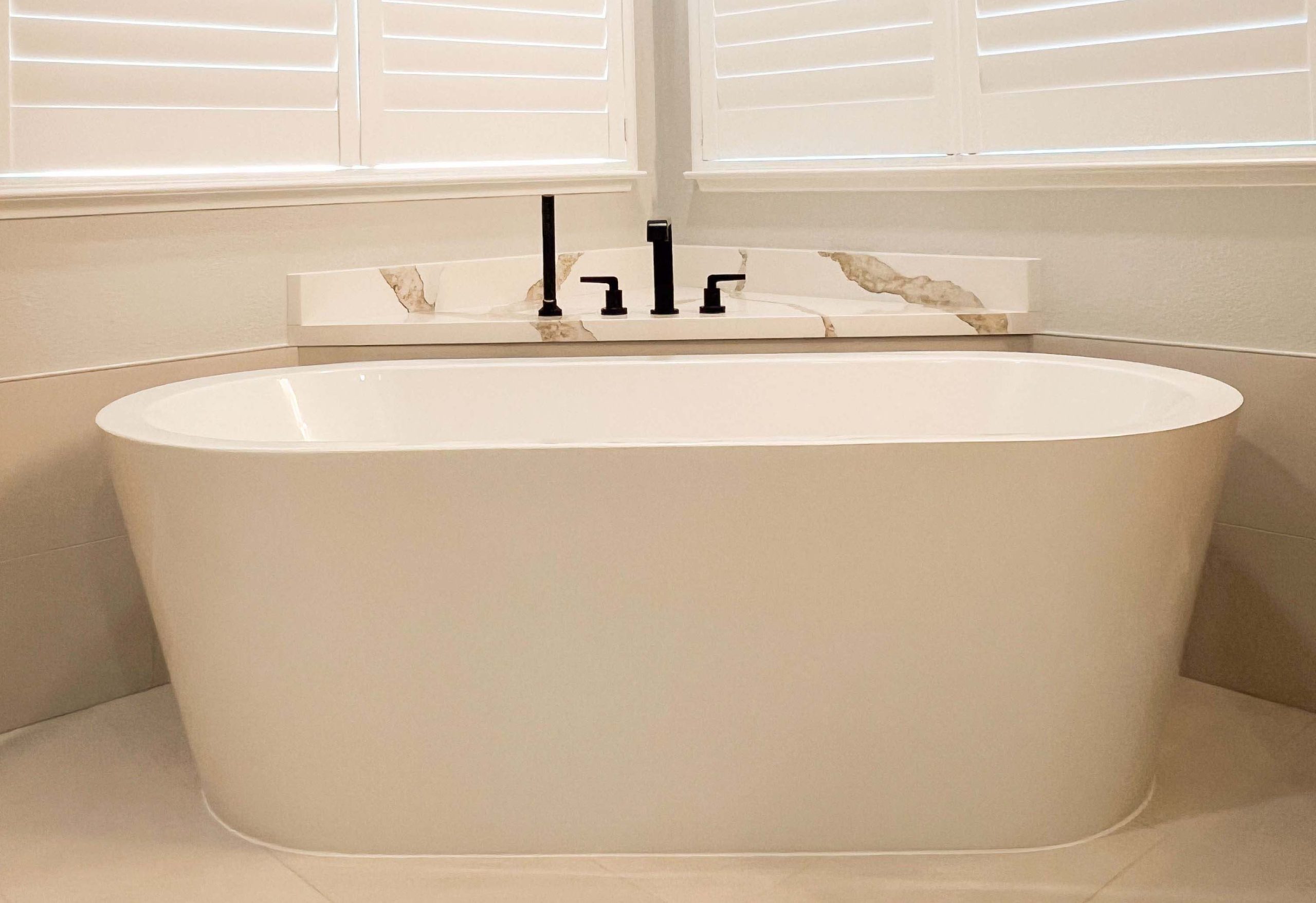 Freestanding tub installed beneath corner plantation shutters after plumbing relocation in a Roseville, CA bathroom remodel.