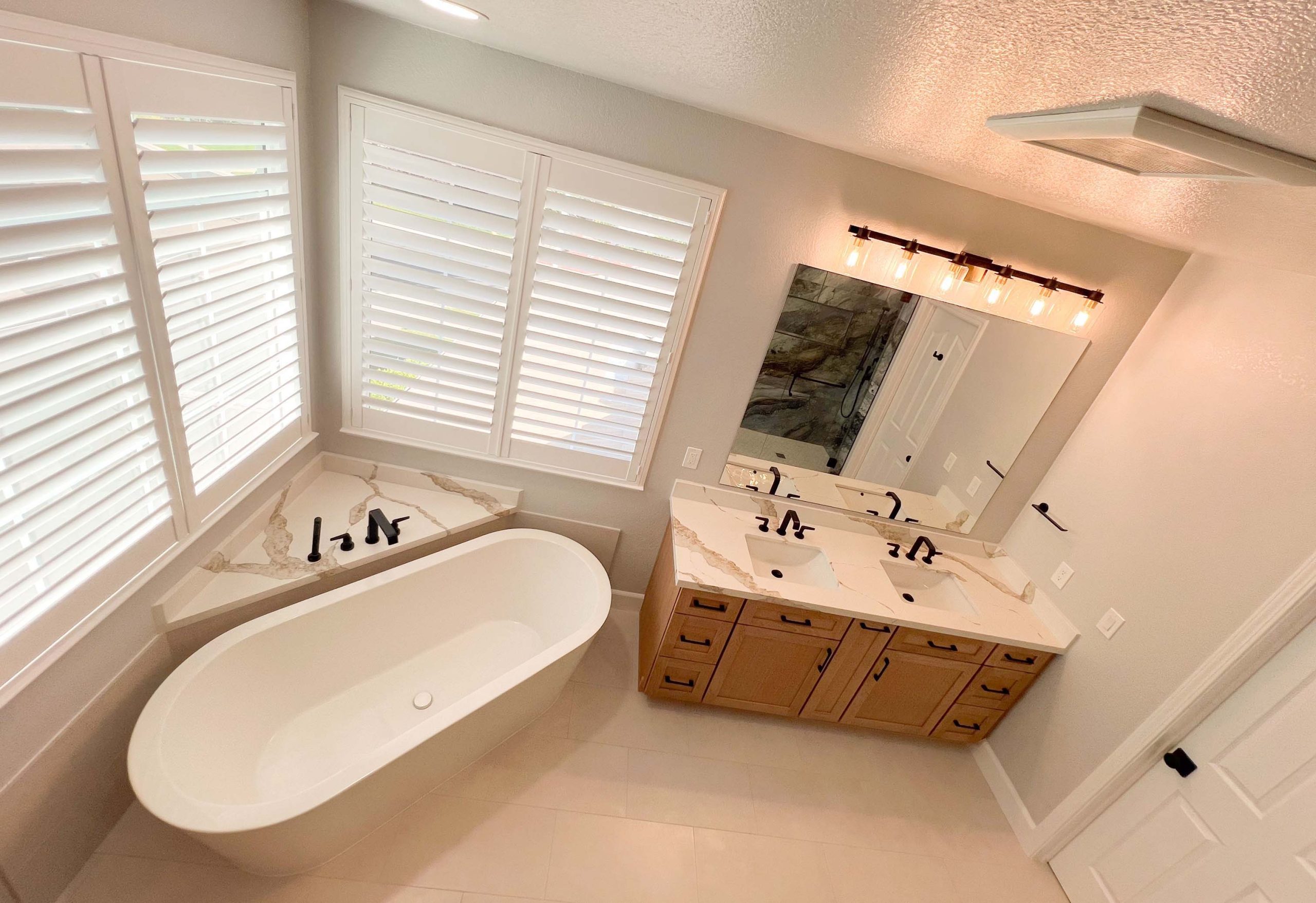 Corner-angle view of a Roseville bathroom remodel highlighting the freestanding tub, quartz countertops, and custom wood double vanity.