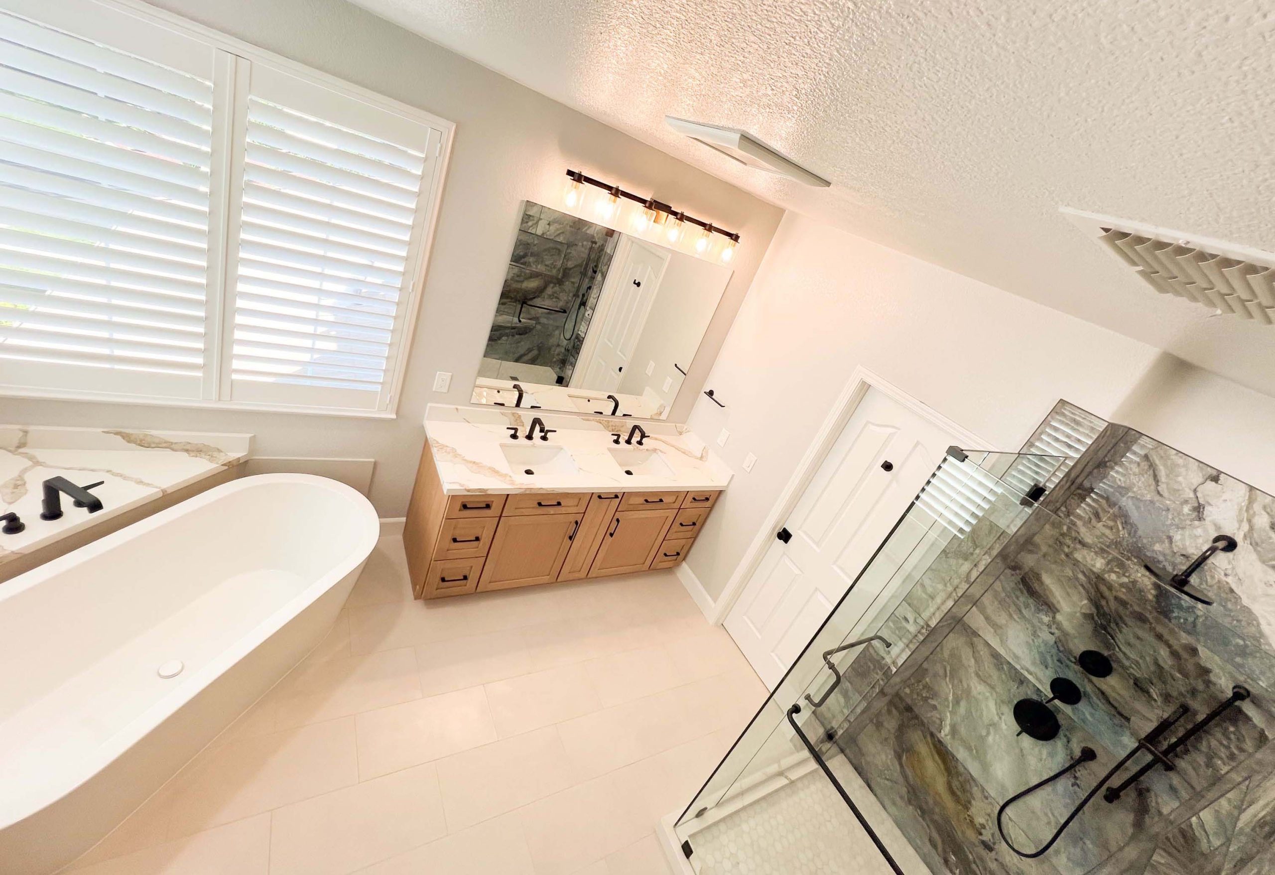 Angled view of a Roseville, CA bathroom remodel featuring a freestanding soaking tub, custom double vanity, and glass-enclosed walk-in shower.