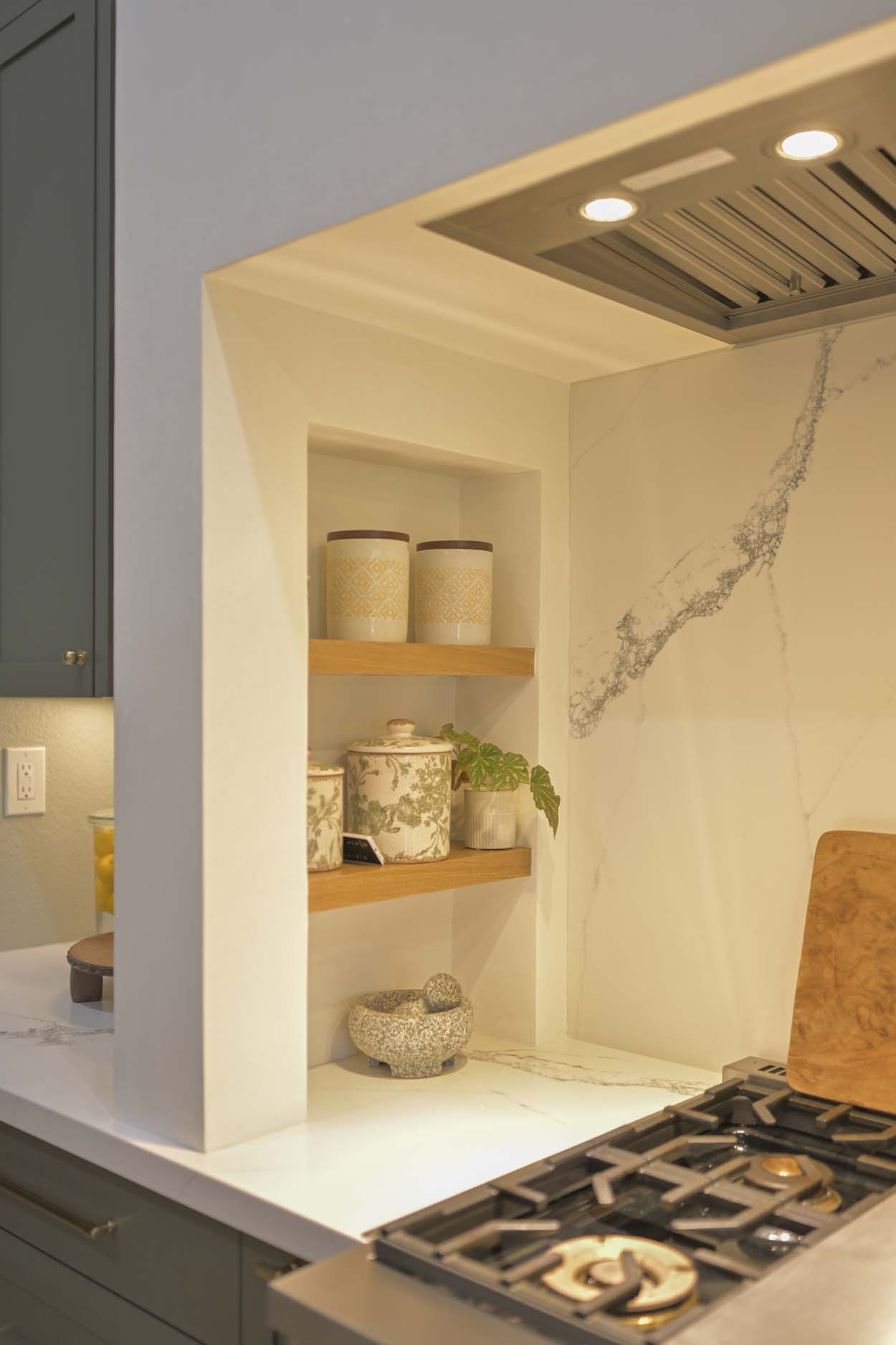 Kitchen remodel in Elk Grove, CA 95758 showcasing a custom plaster range hood, open wood shelving, and slab backsplash detail.